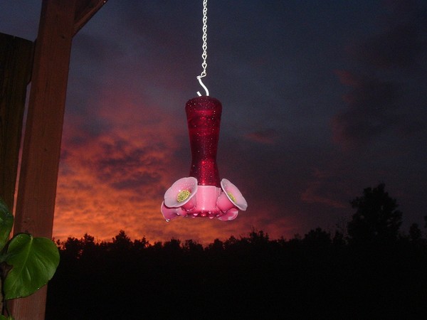 Red hummmingbird feeder against the red sky